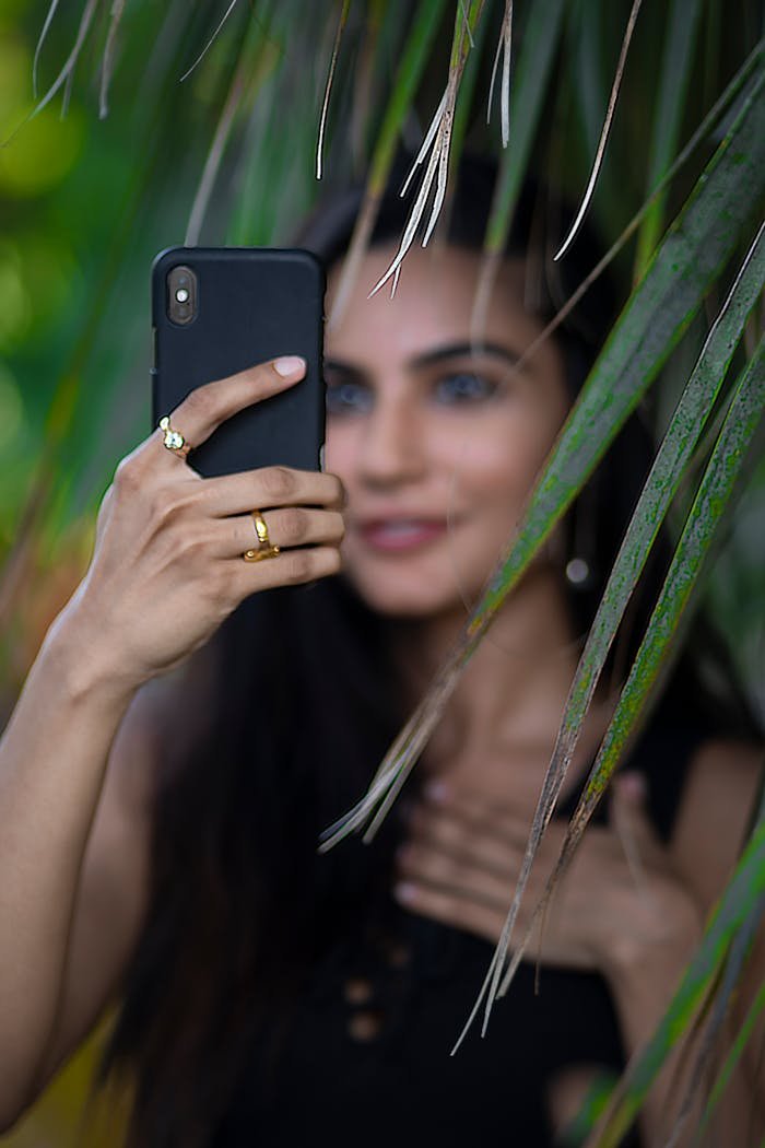 services-04 A woman capturing a selfie on her smartphone amidst vibrant greenery, showcasing modern technology and lifestyle.