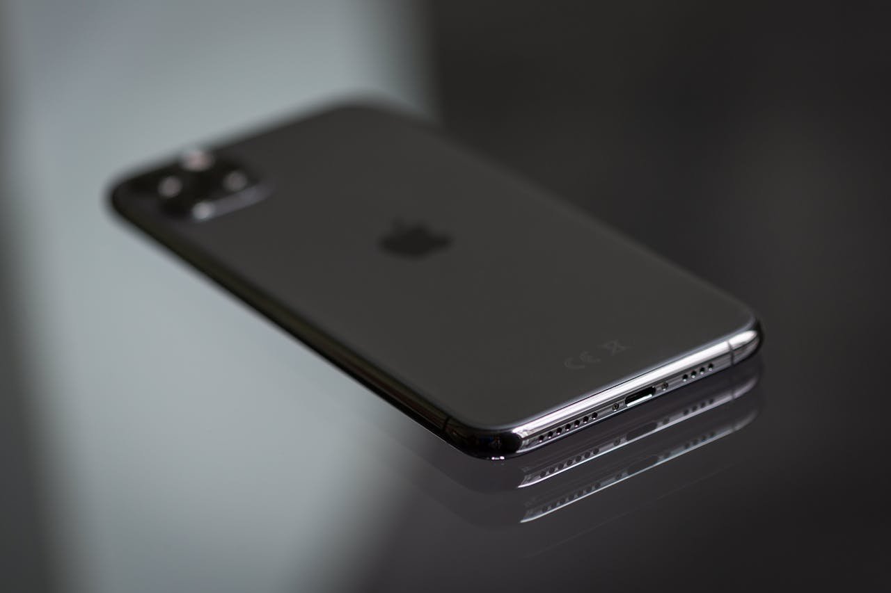 Close-up of a black smartphone on a shiny reflective surface, highlighting its sleek design.
